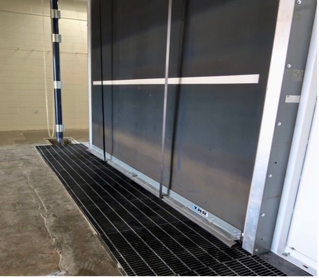 A metal grating at the base of a large doorway with a steel panel, possibly for drainage.