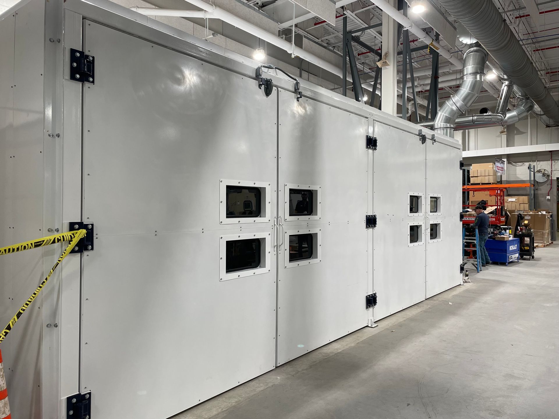 Large white industrial noise enclosure with multiple access panels in a factory setting.