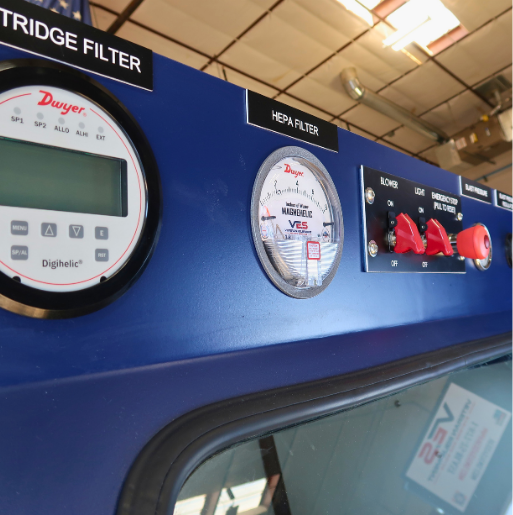 Close-up of VES blast cabinet control panel with cartridge filter gauge, HEPA filter gauge, emergency stop, and lighting controls