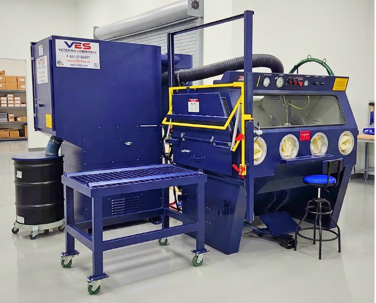 VES blast cabinet system with integrated dust collection, vertical take off door, front work platform, safety railing, and operator controls in a clean industrial facility