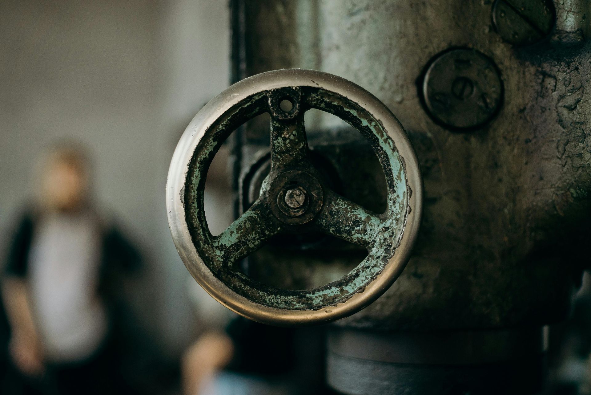 Rusty metal wheel, part of machinery, with a blurred person in the background.