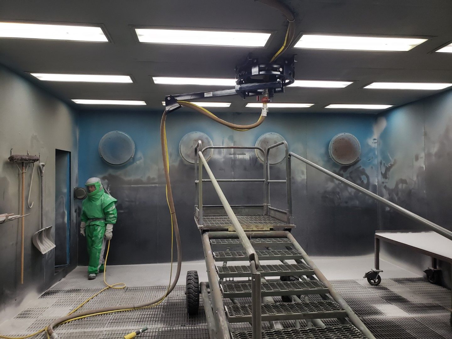 A person in a hazmat suit inside a spray booth. A robotic arm and stairs are also present.