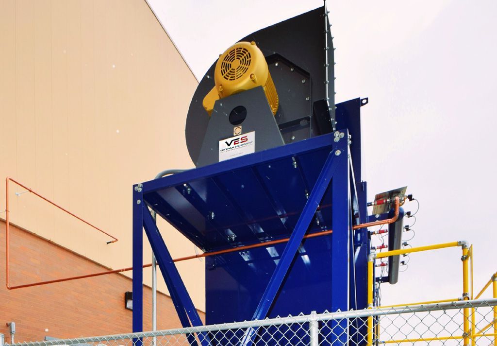 Blue industrial exhaust fan on a metal structure with a yellow motor, outdoors.
