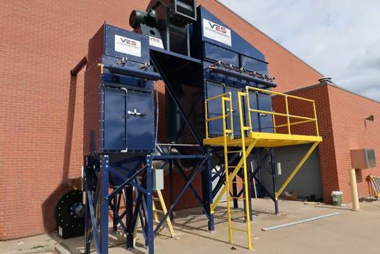 Blue industrial dust collection system with yellow access platform, mounted on a brick building.