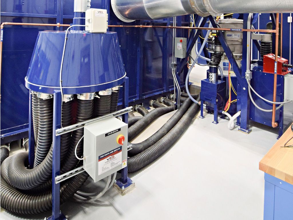 Blue industrial machinery with multiple flexible hoses and control panel in a factory setting.