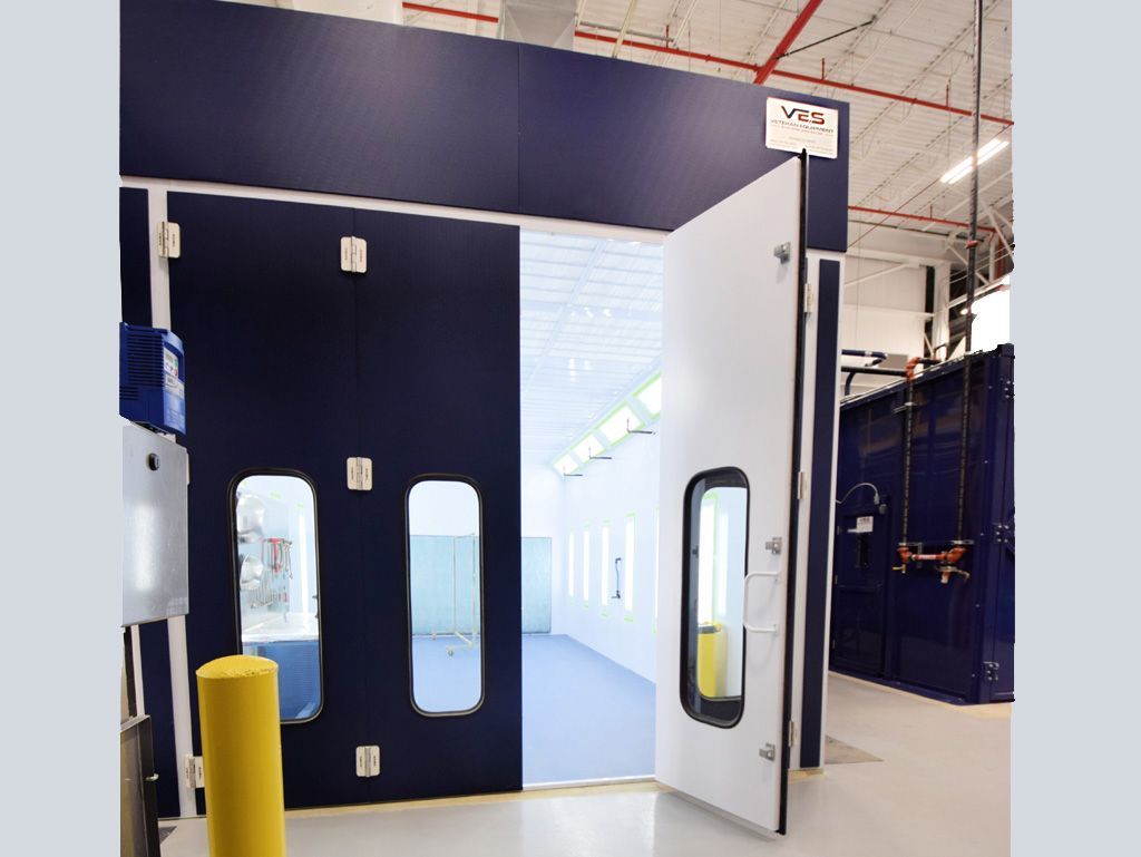 Blue and white paint booth with open door, in a factory setting.