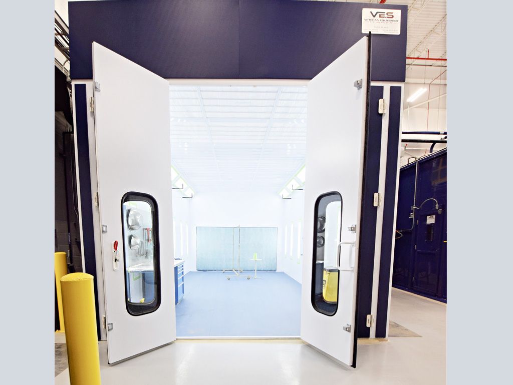 Open white doors of a paint booth in a workshop, blue and white tones.