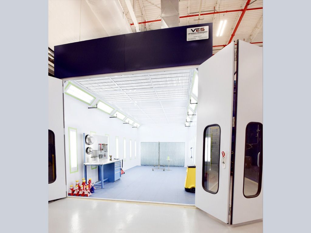 White and black auto paint booth inside a large industrial building.