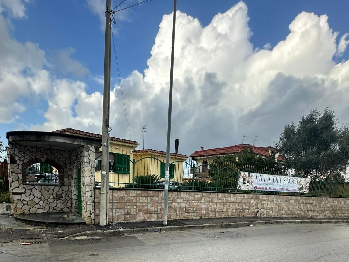 Edifici con muri in pietra e un cielo nuvoloso sopra; uno striscione è appeso sulla parete destra.