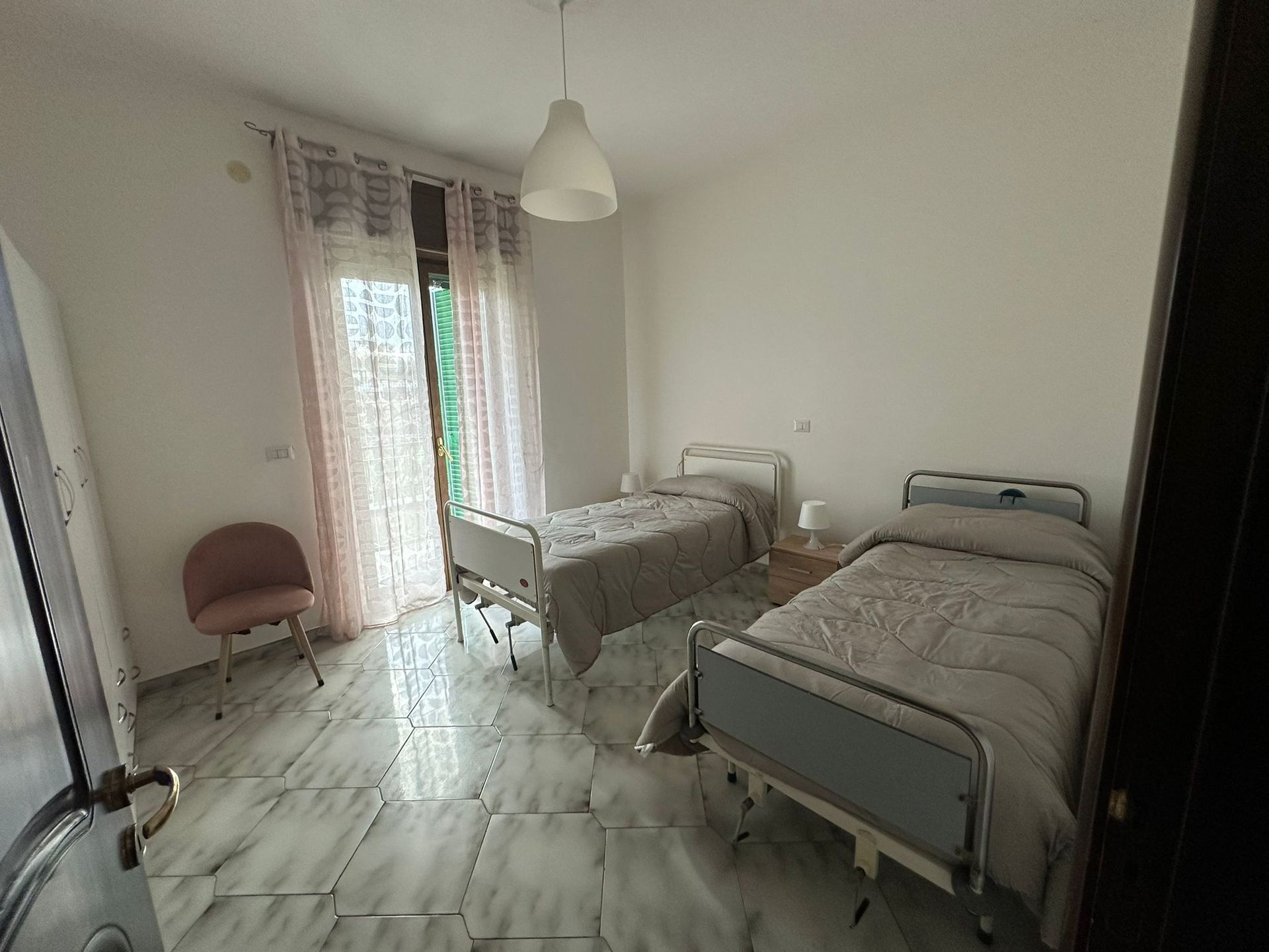 Due letti d'ospedale in una stanza luminosa con pavimenti in marmo e una porta che conduce all'esterno.