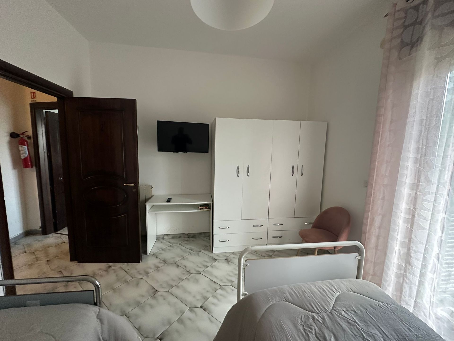 Una camera da letto con due letti, armadio bianco, scrivania, TV e porte aperte verso altre stanze.