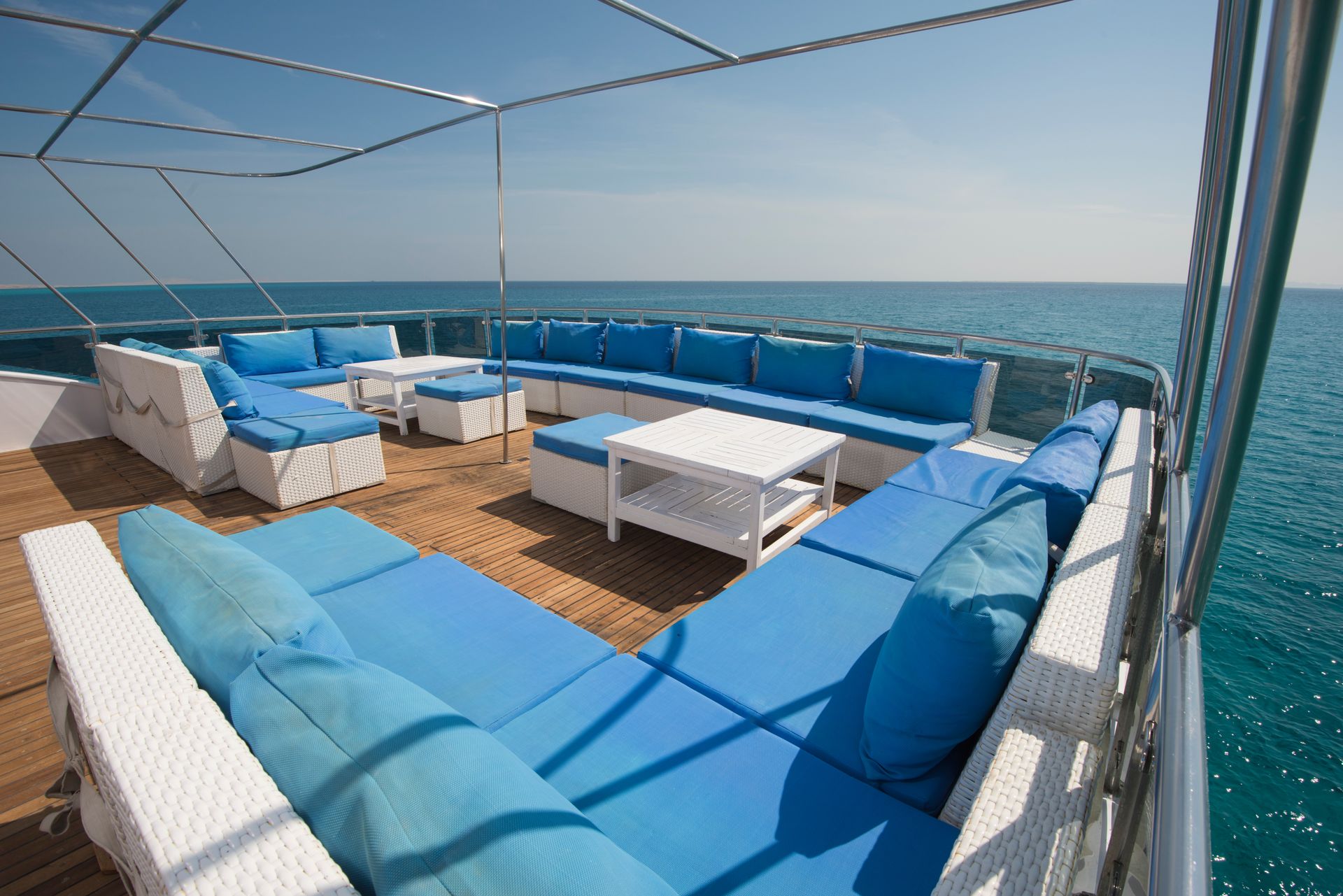 Large white outdoor lounge set with blue upholstered cushions on deck of boat on the ocean