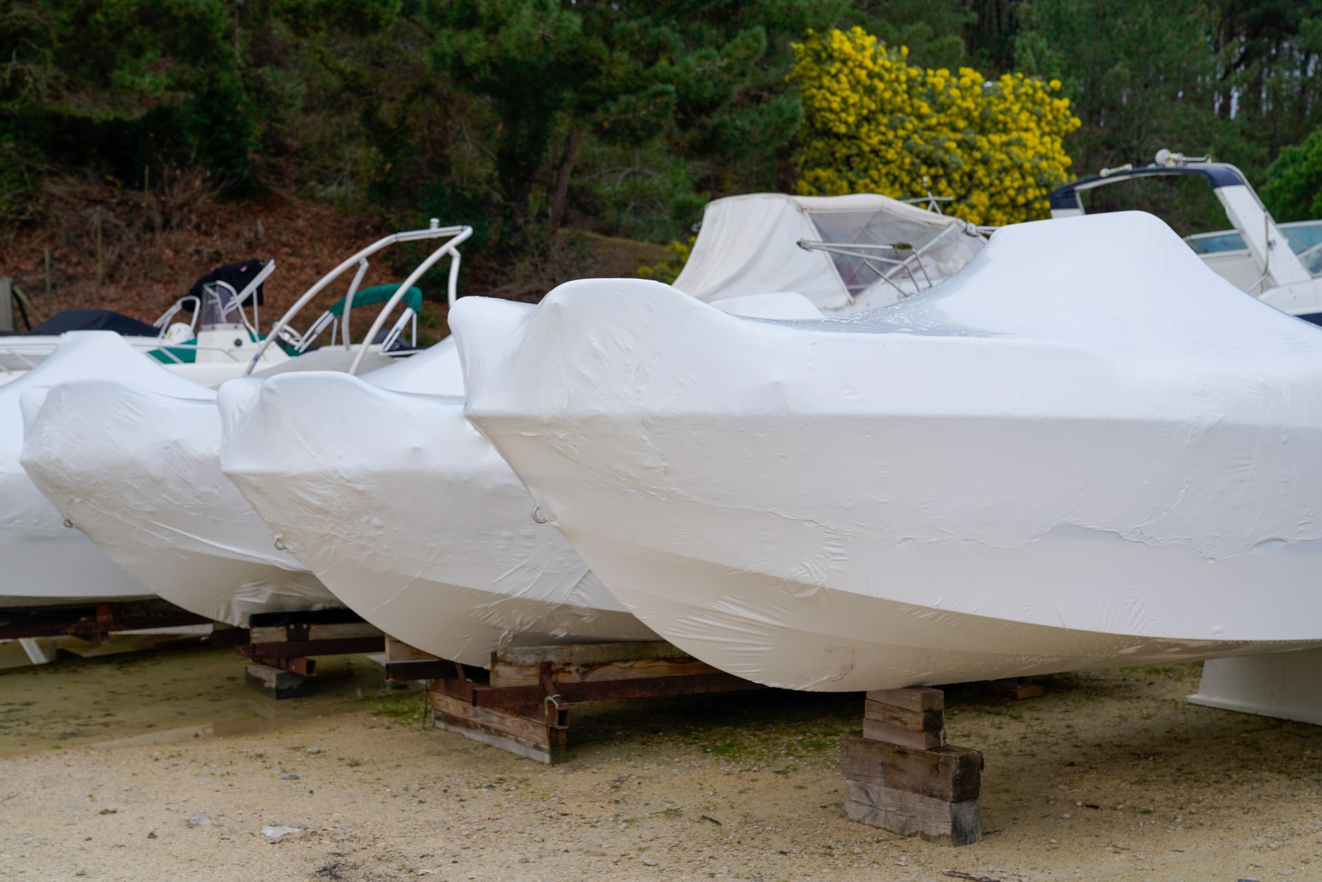 Four small boats stored on land fully covered with white boat covers