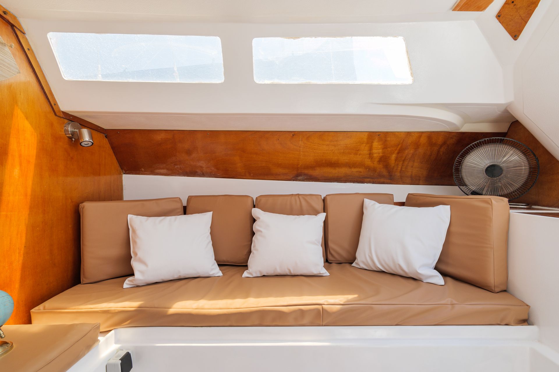 Seating area inside of boat with brown upholstered cushioning and white scatter cushions