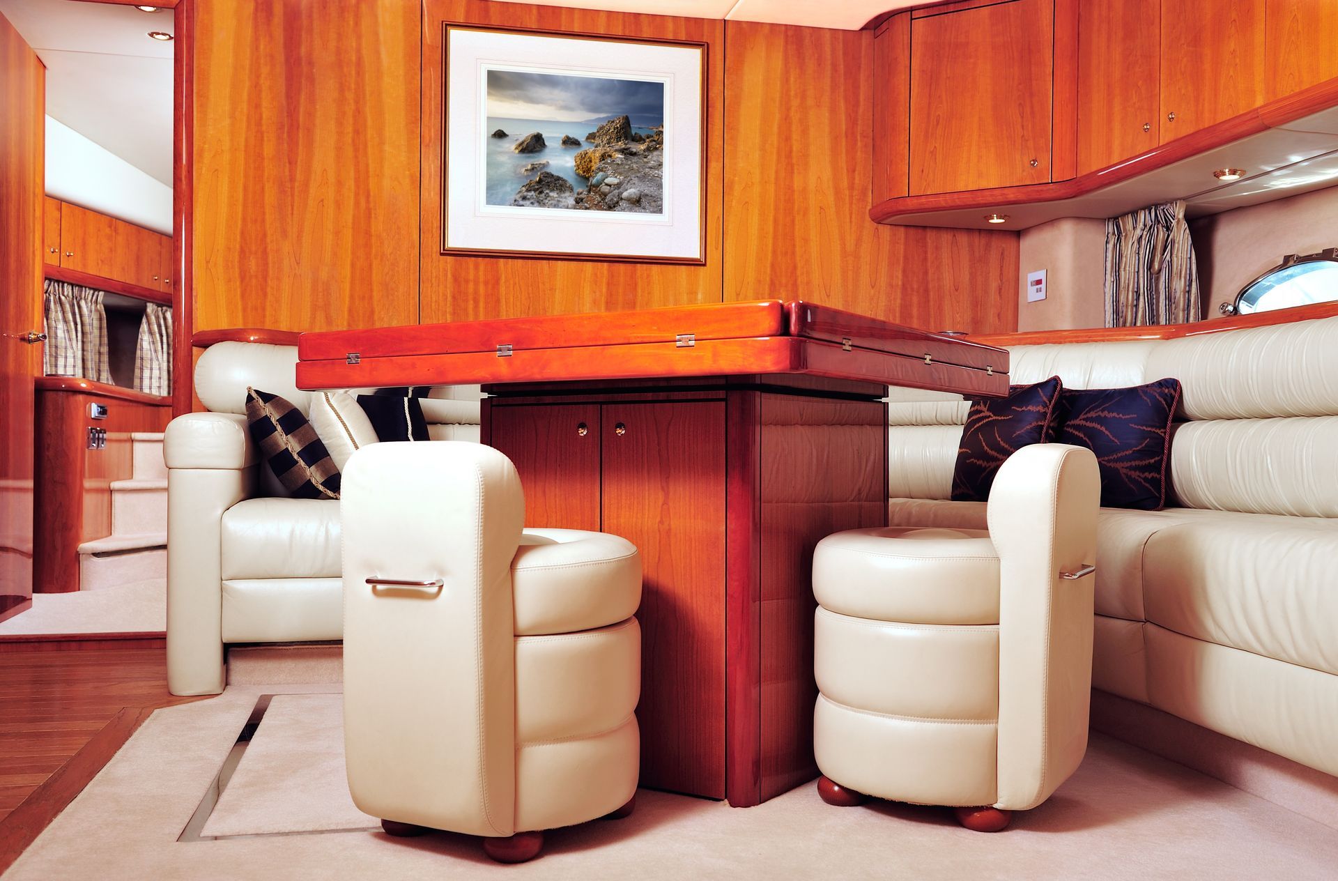 Cream leather upholstered seating area and small chairs around small wooden table inside a boat