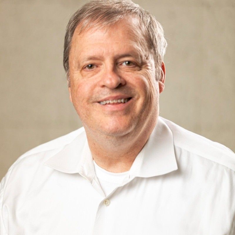 Man smiling, wearing a white shirt, against a neutral background.