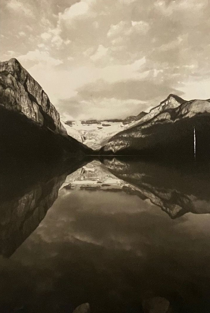 Mountains reflected in calm lake water under cloudy sky.