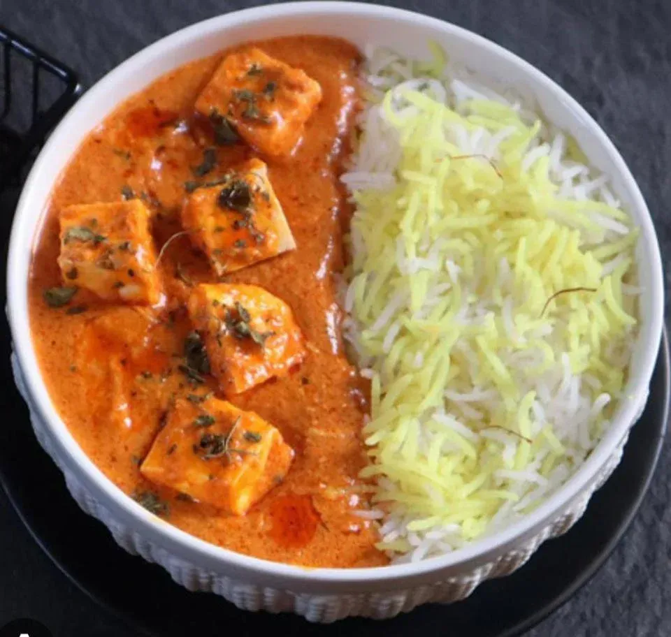 Paneer butter masala with saffron rice in white bowl.