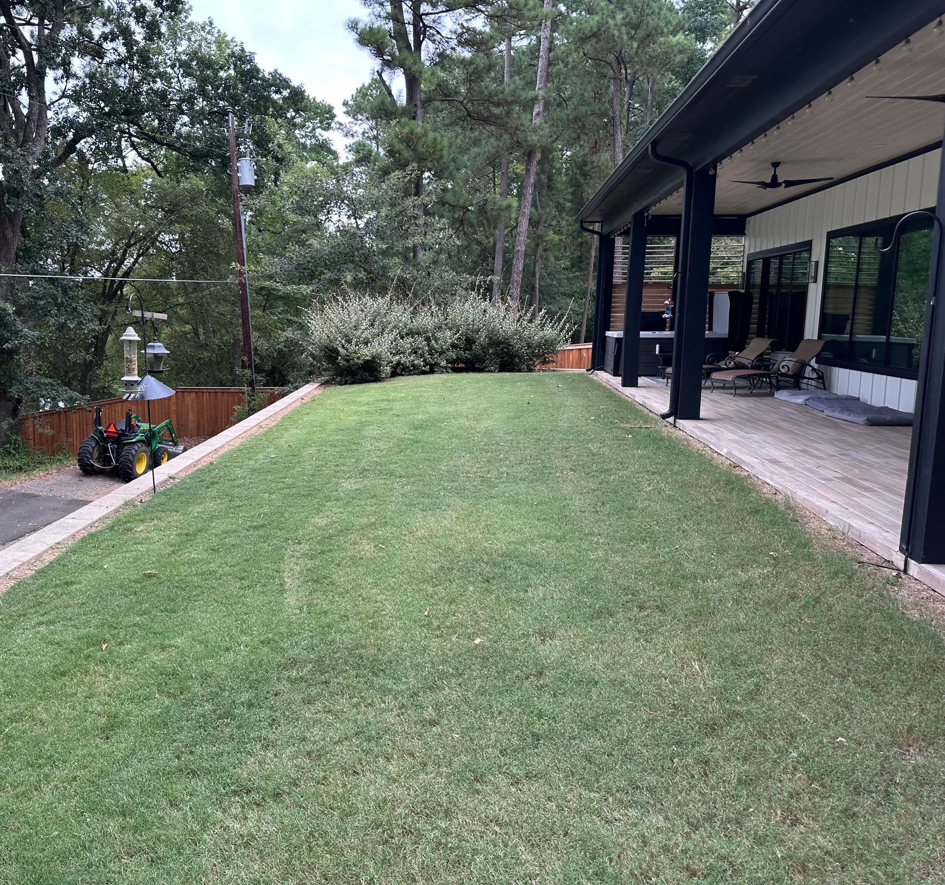 Lush green lawn with a low retaining wall, adjacent to a house with a covered porch.