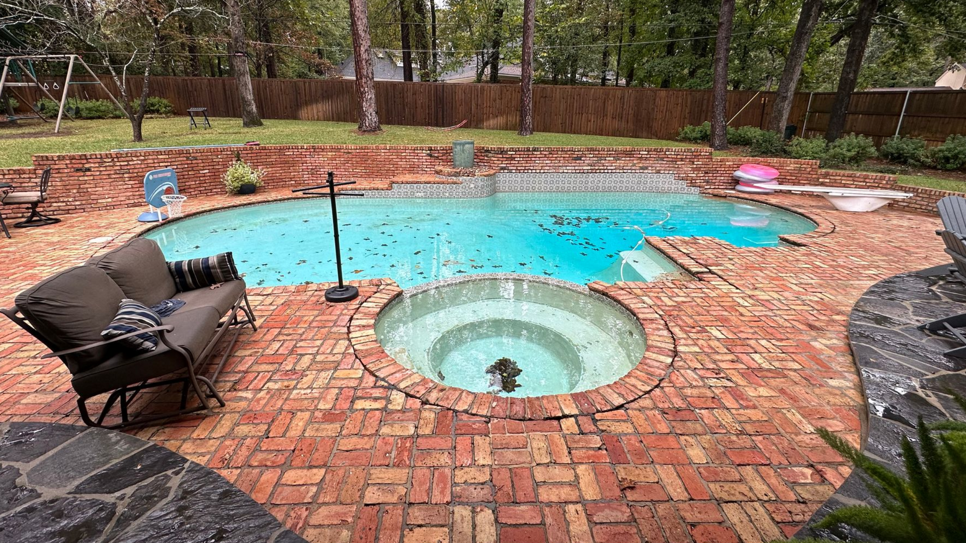 Backyard pool with brick patio, sofa, and a hot tub.