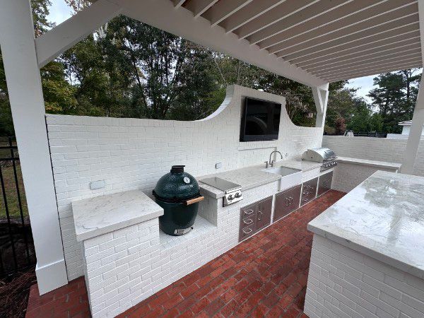 Outdoor kitchen with white brick, gray countertops, grill, sink, and TV.