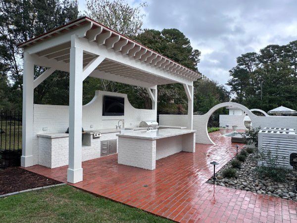 Outdoor kitchen with white brick structure, grill, and red brick flooring. Overcast day.