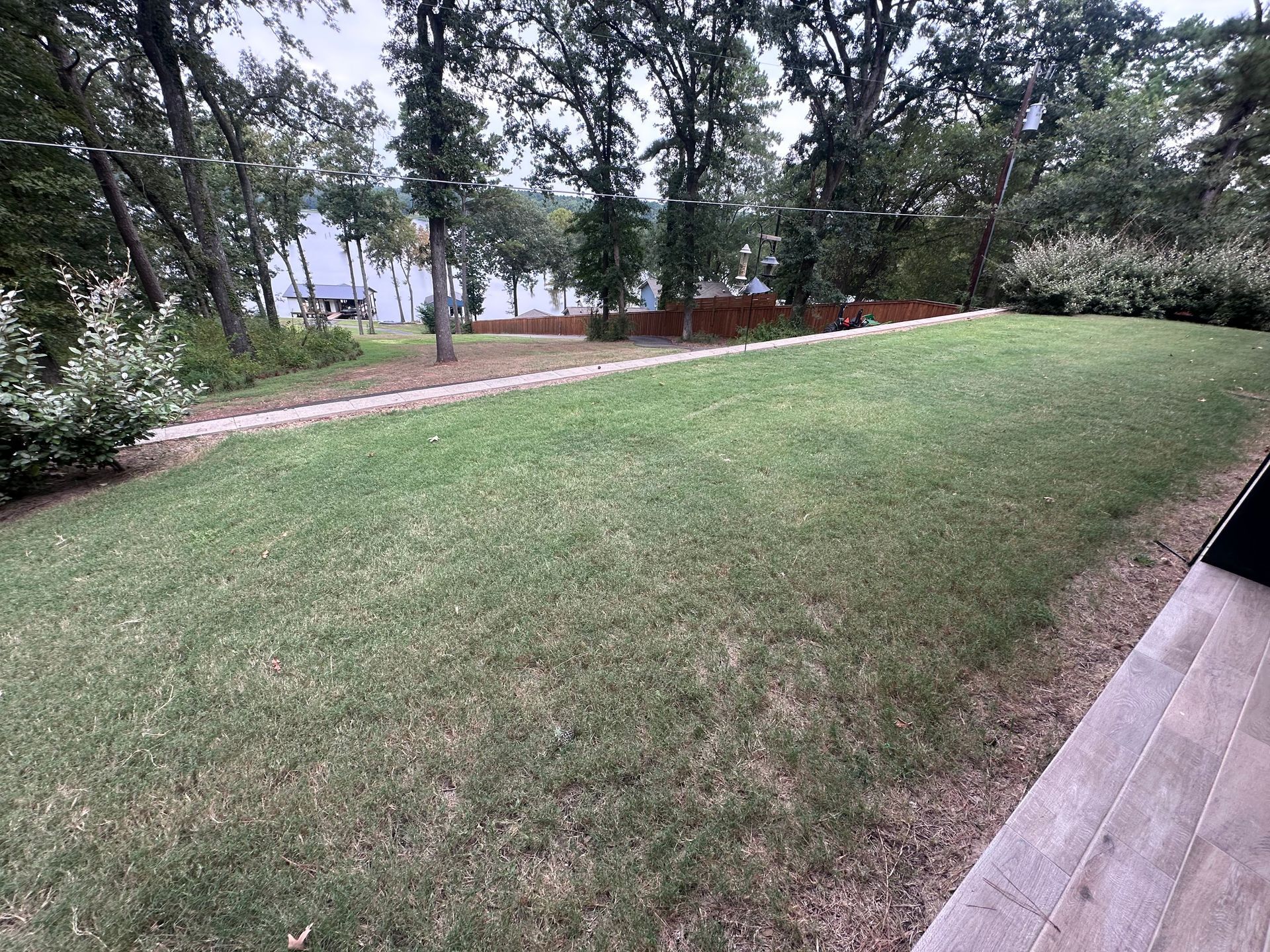 Green lawn with trees and a pathway in the background. Stone patio on the right.