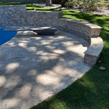 A curved stone retaining wall borders a patio near a swimming pool, featuring a diving board extending over the water.
