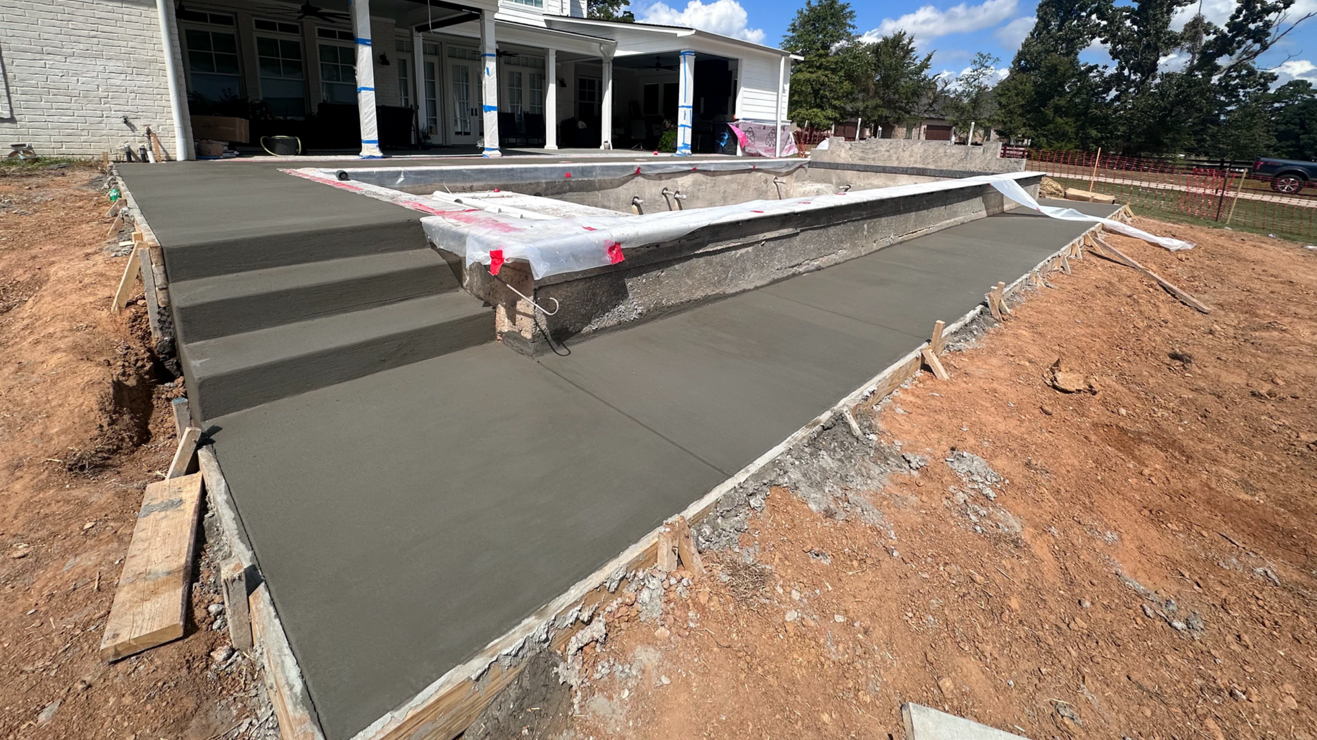 Newly poured concrete steps and walkway leading to a pool under construction.