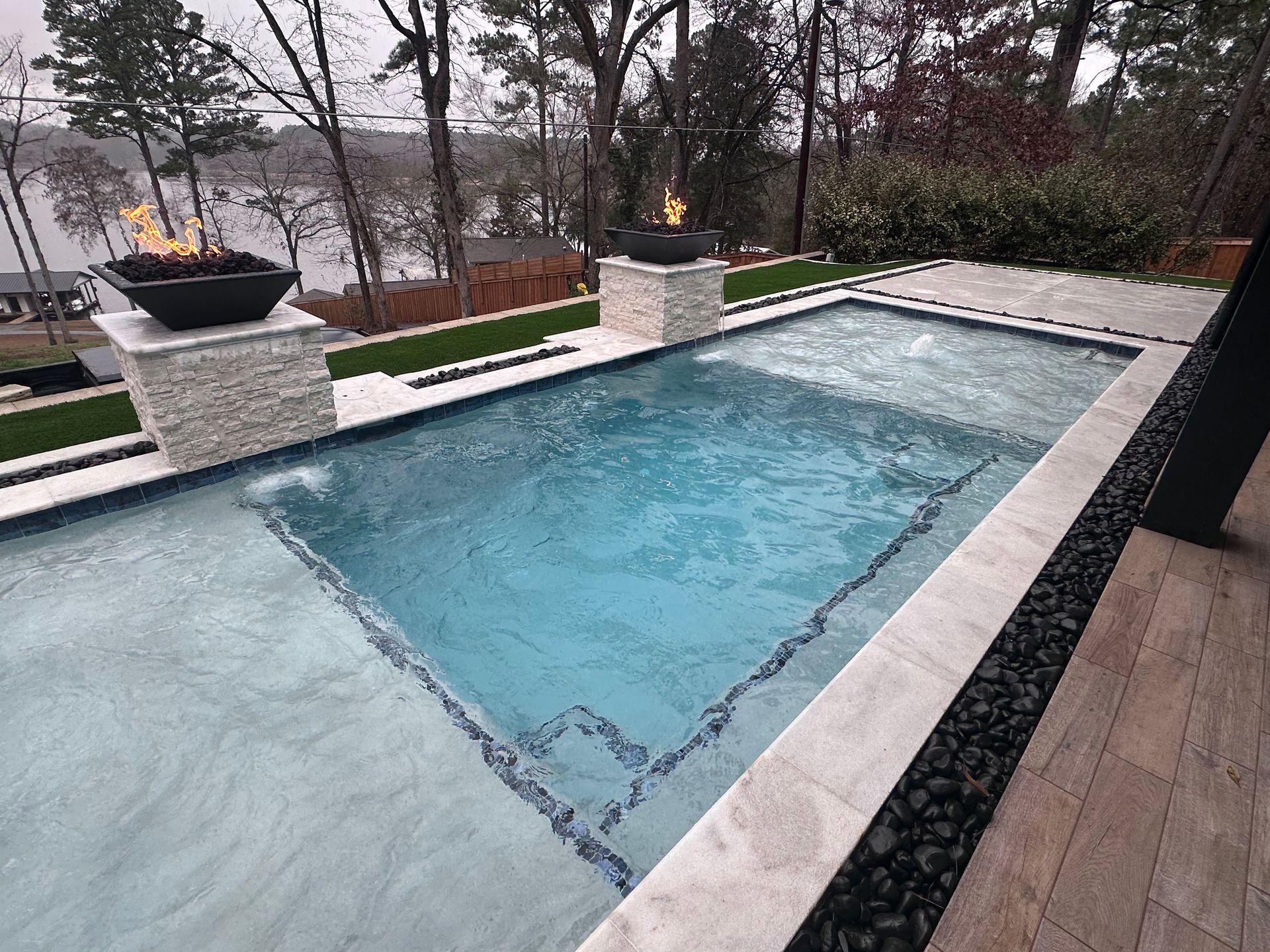 Rectangular outdoor pool with blue water, stone deck, and fire bowls on a cloudy day