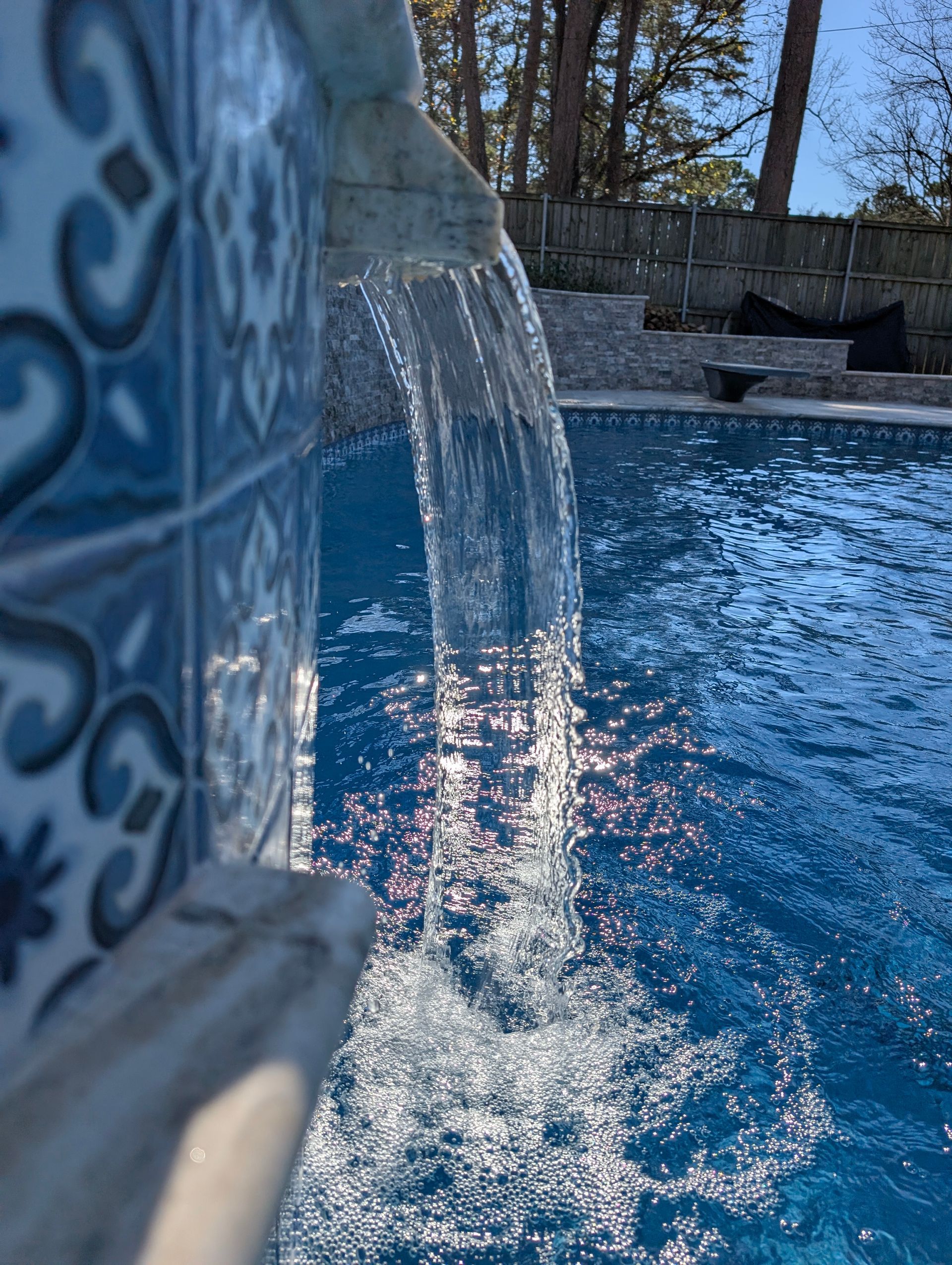 Water cascading into a blue-tiled pool with sunlight reflecting on the surface.