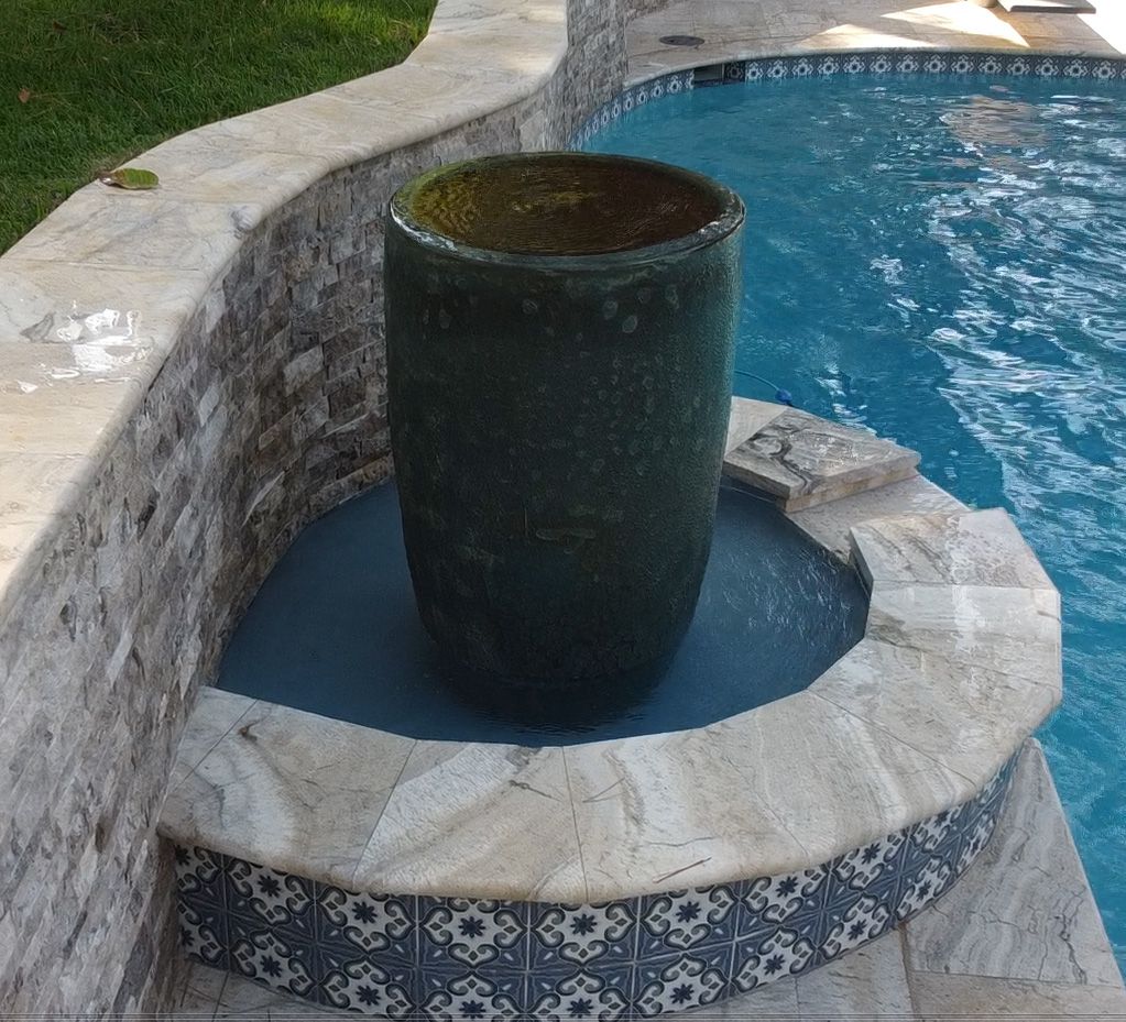 Large green planter in a pool with stone and tiled surroundings.