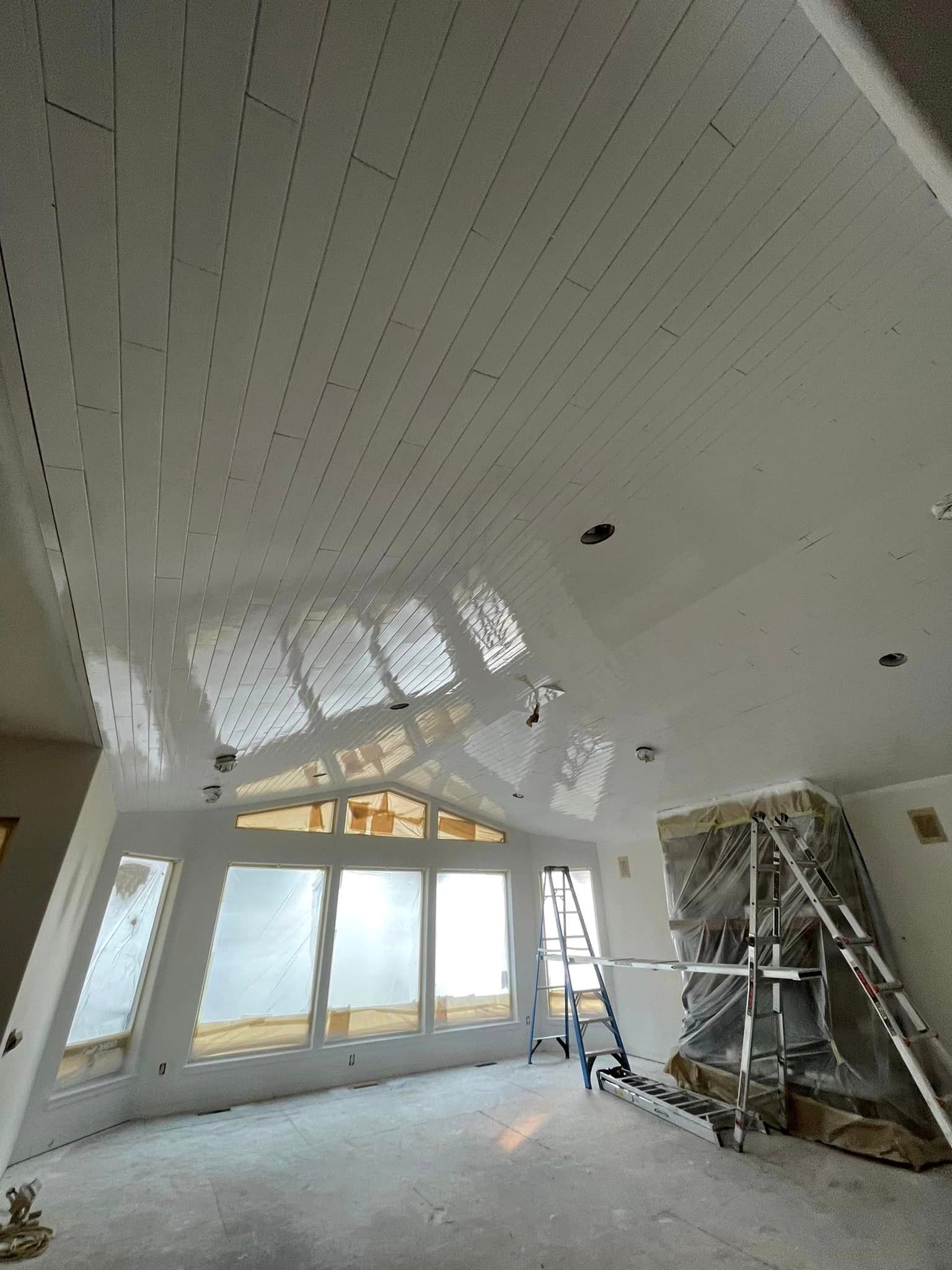 Interior view of a room under renovation featuring a white vaulted tongue-and-groove ceiling and a stone fireplace.