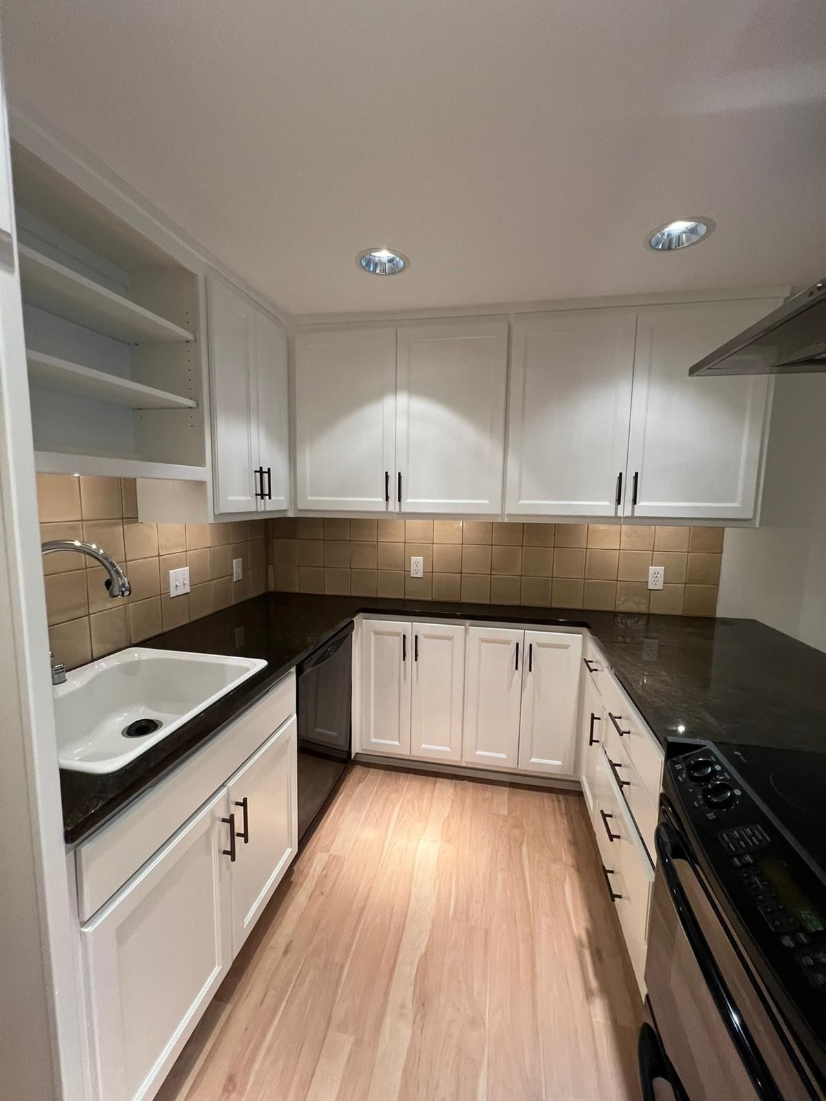 A U-shaped kitchen with white cabinets, dark countertops, beige backsplash, and light wood flooring.