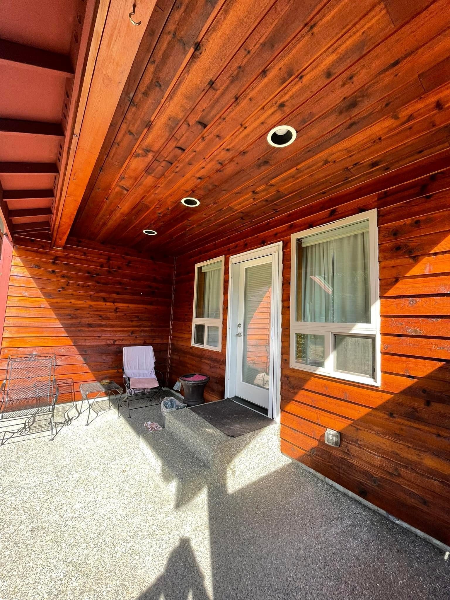 A gravel patio area in front of a house with warm-toned horizontal wood siding and recessed ceiling lighting.