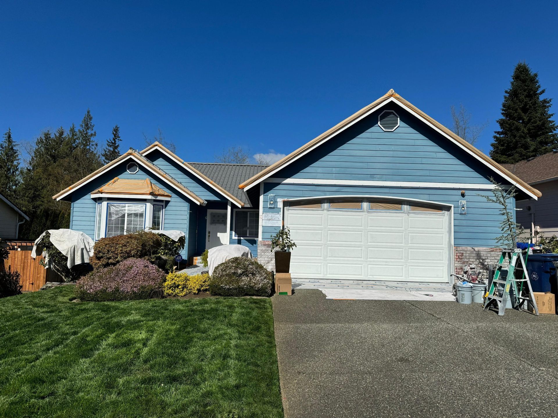A single-story blue house with a white garage door, stone accents, and a front lawn under a clear blue sky.