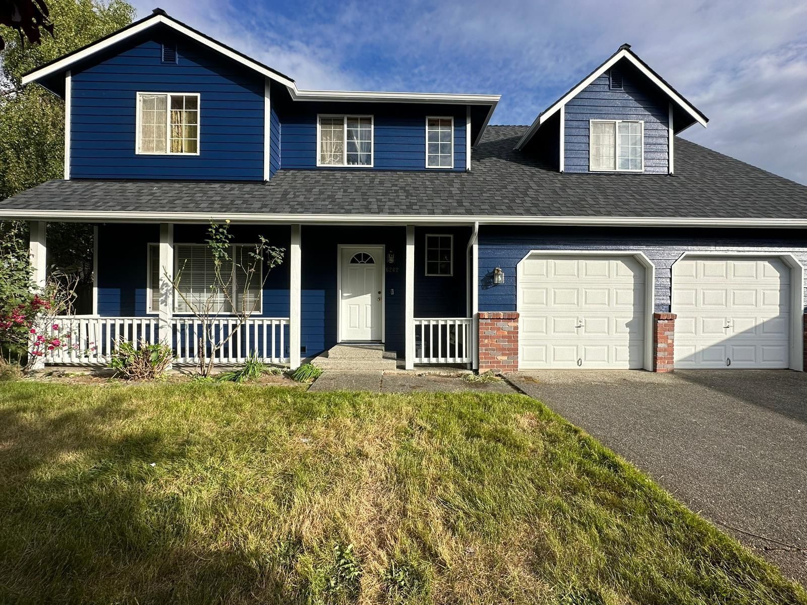 A two-story blue house with a white front porch, a gravel driveway, and a two-car garage.