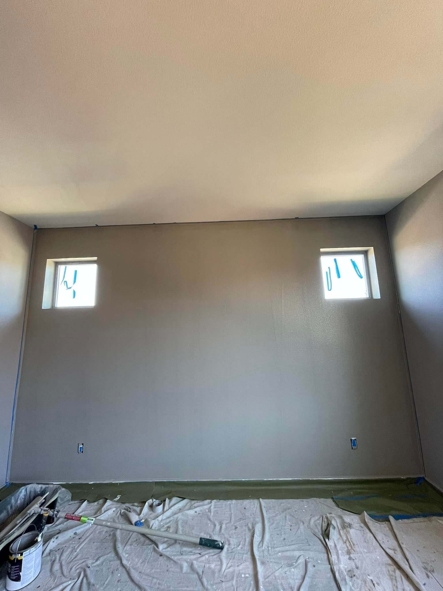A freshly painted gray wall with two square windows, beneath a textured ceiling in a room under construction.