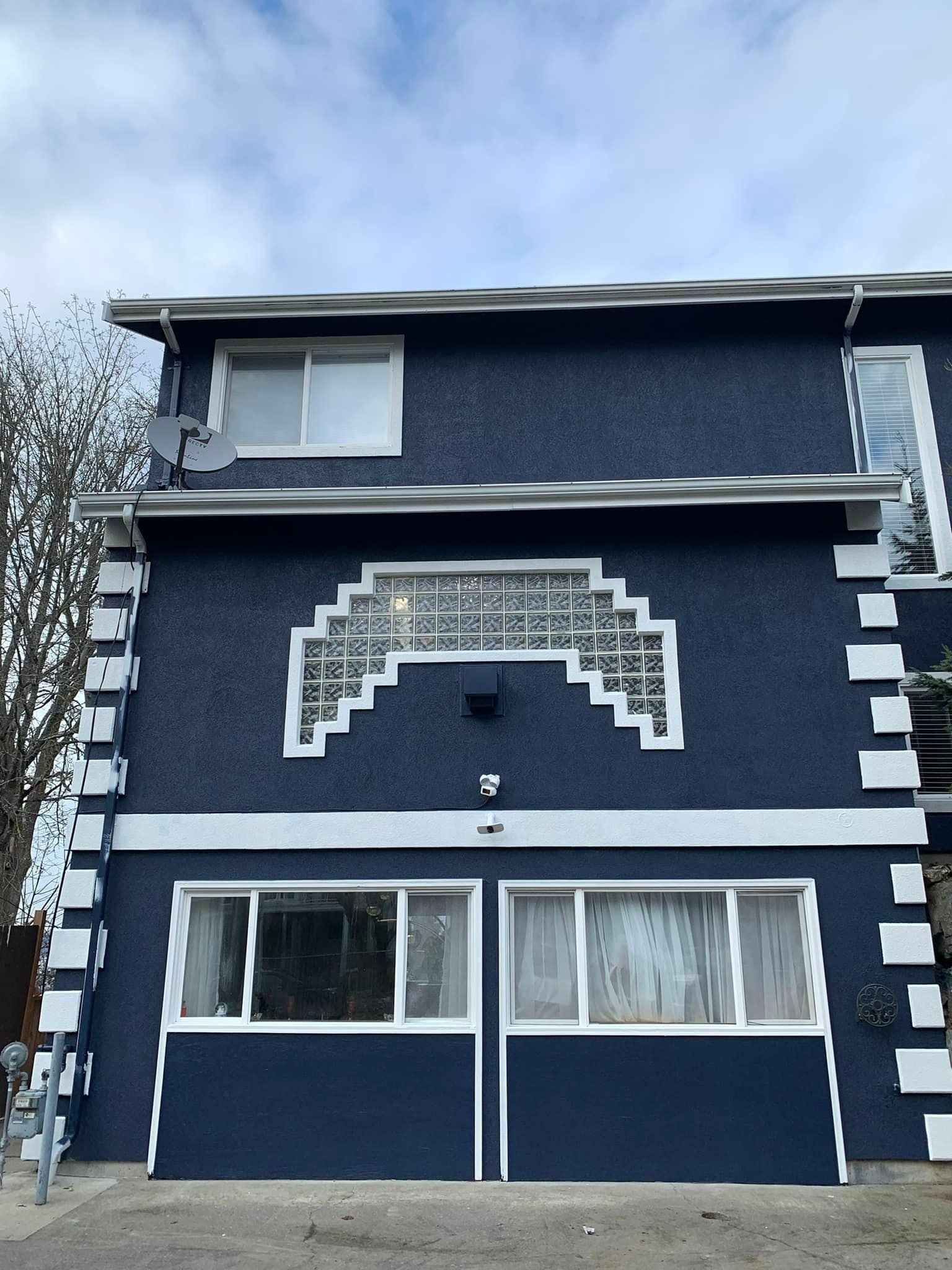 A two-story dark blue building with a stepped-arch glass block window design and white corner accents.