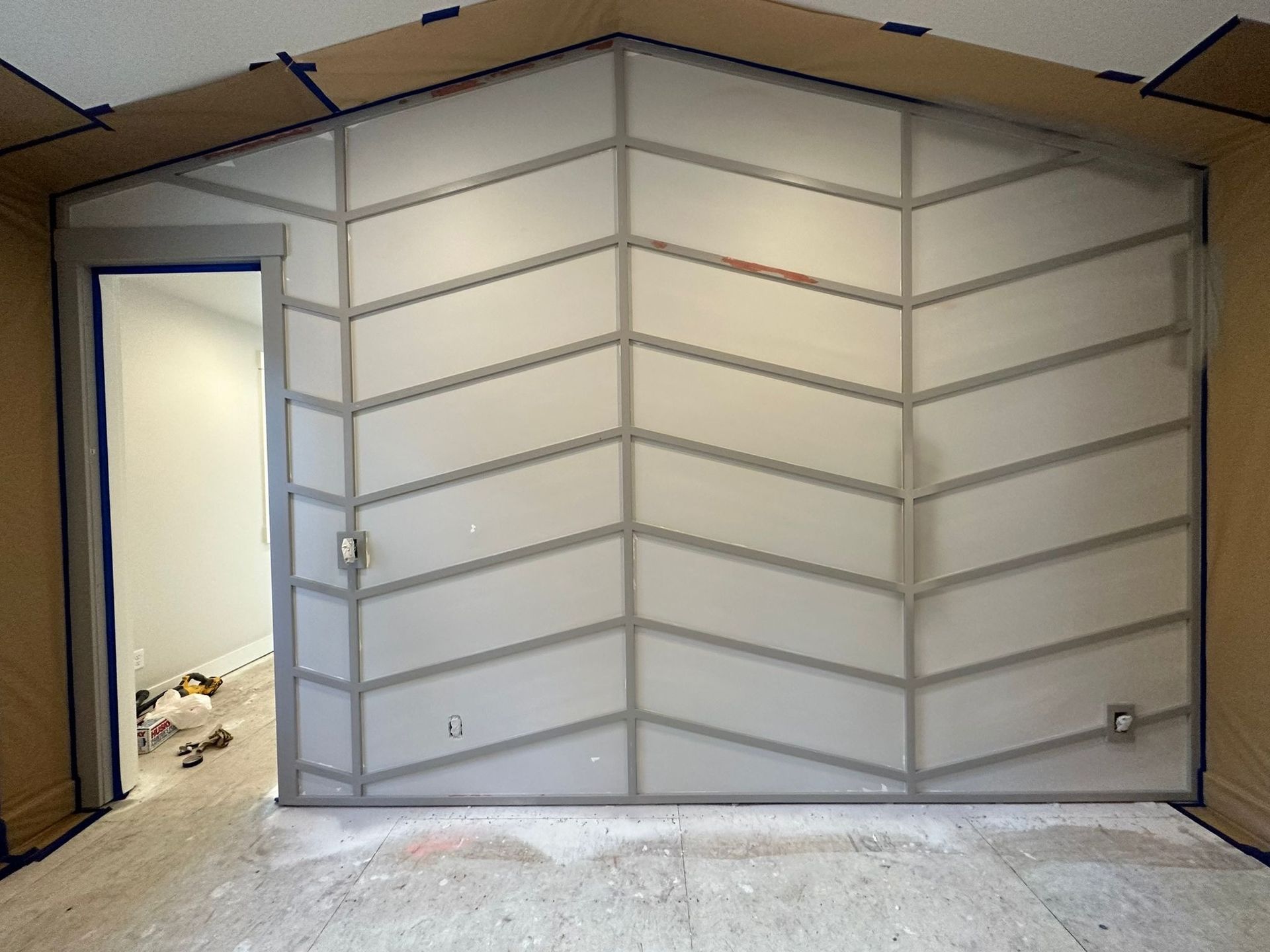 An interior wall in progress featuring a light gray chevron wood trim pattern on a plain wall with an open doorway.