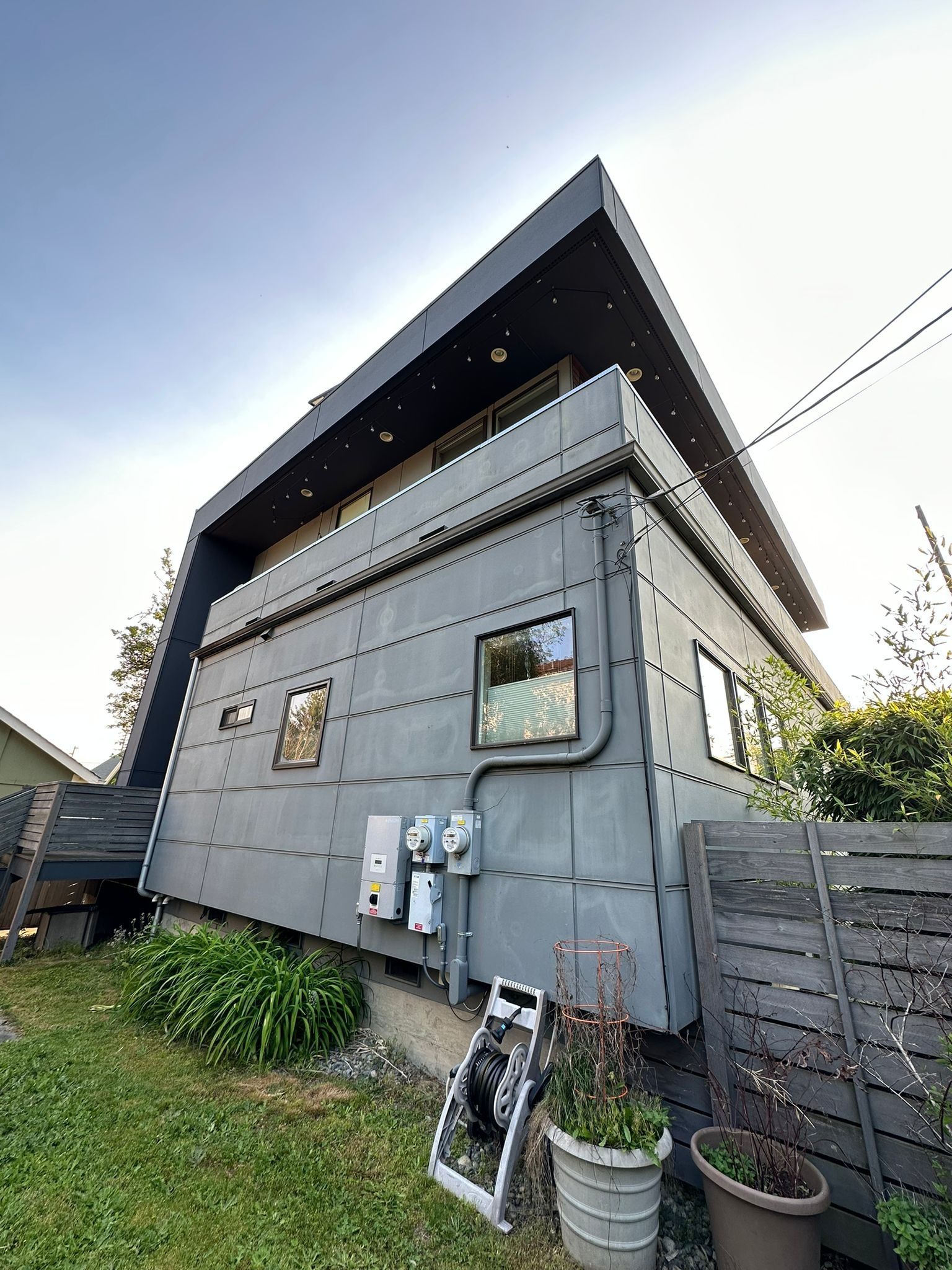 Low-angle view of a modern two-story home with gray rectangular siding, black trim, and a prominent overhanging roof.