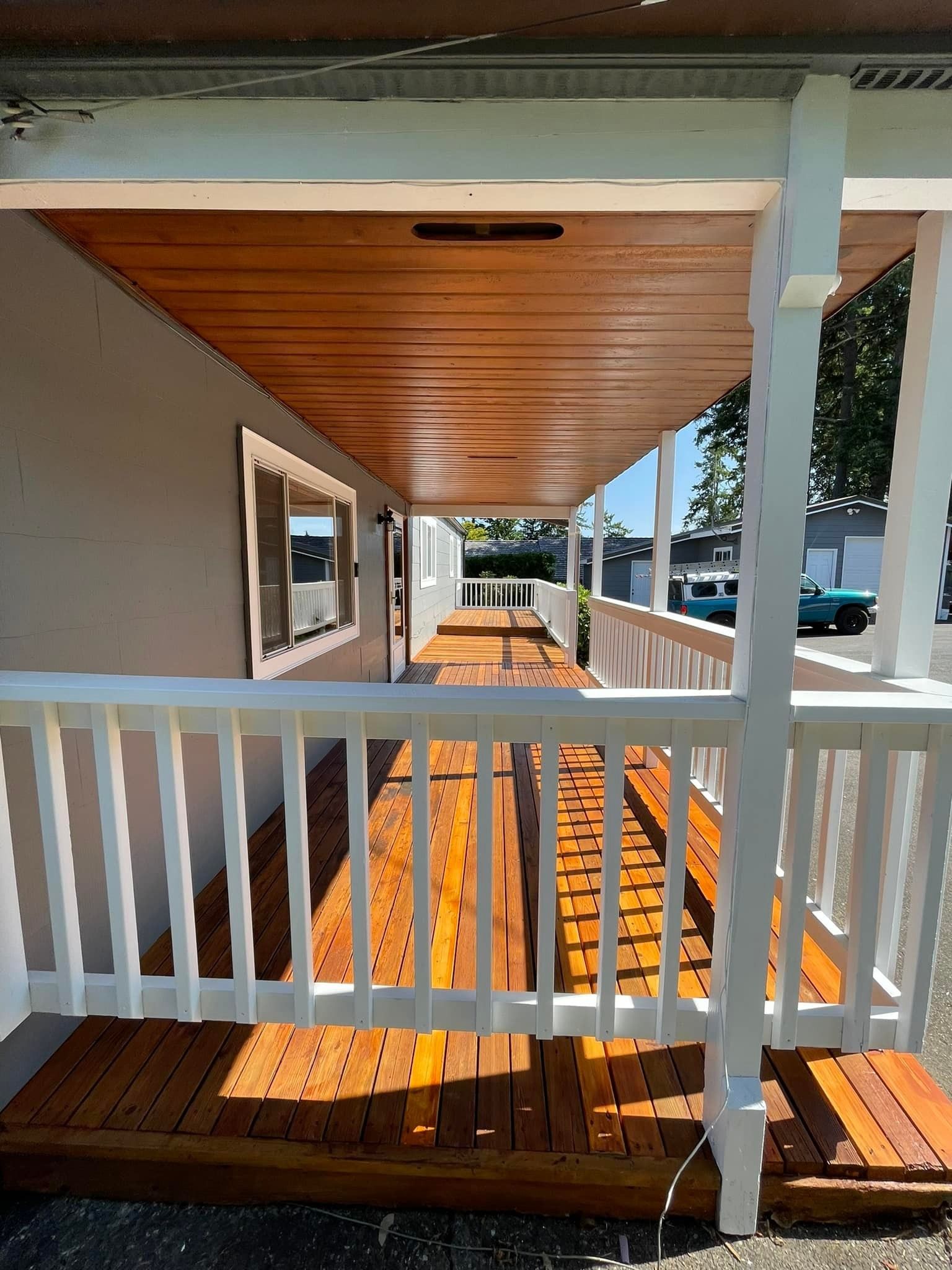 A wooden porch with a white railing and a wooden ceiling, viewed from the front entrance area.