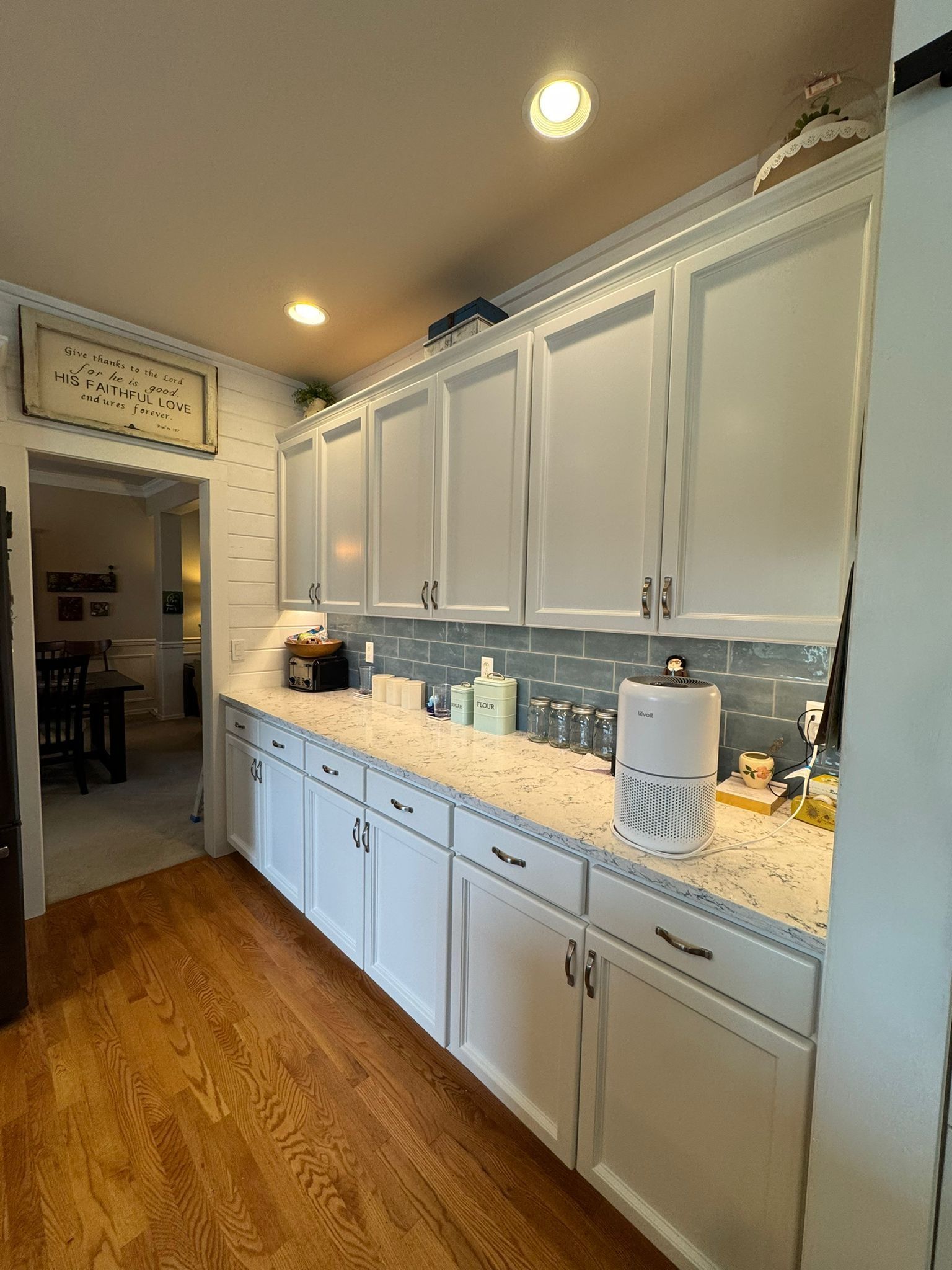 A hallway built-in buffet with white cabinets, speckled countertops, a gray tiled backsplash, and light hardwood floors.