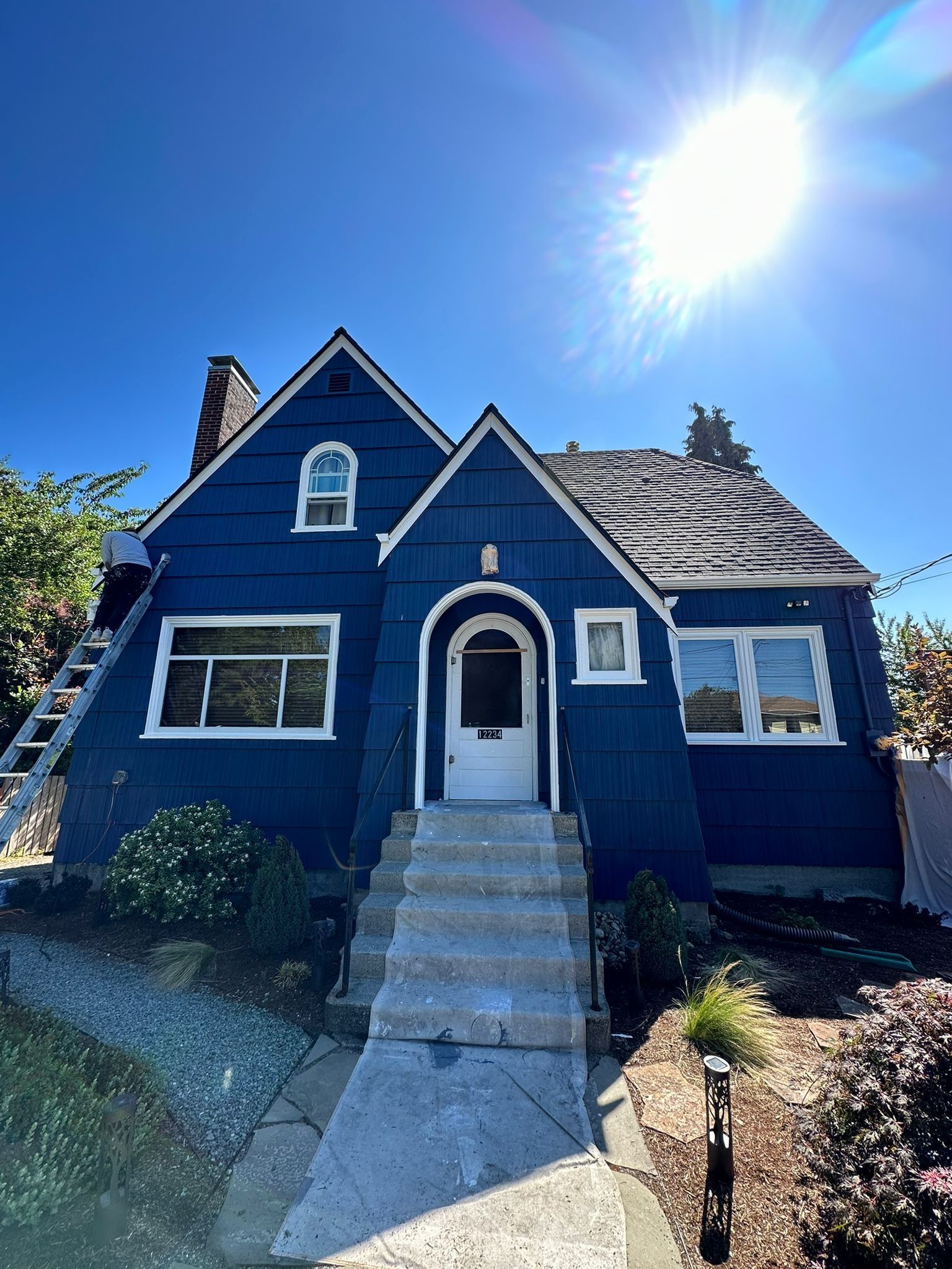 A navy blue, two-story house with a white front door, stone steps, and a bright, sunlit sky.