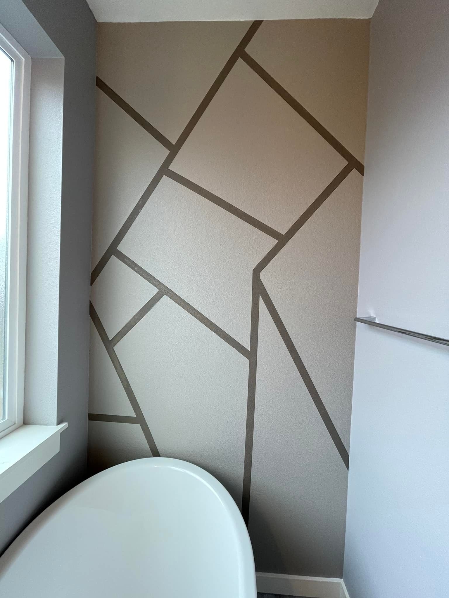 An accent wall behind a bathtub featuring an abstract, geometric pattern of tan shapes separated by dark brown lines.