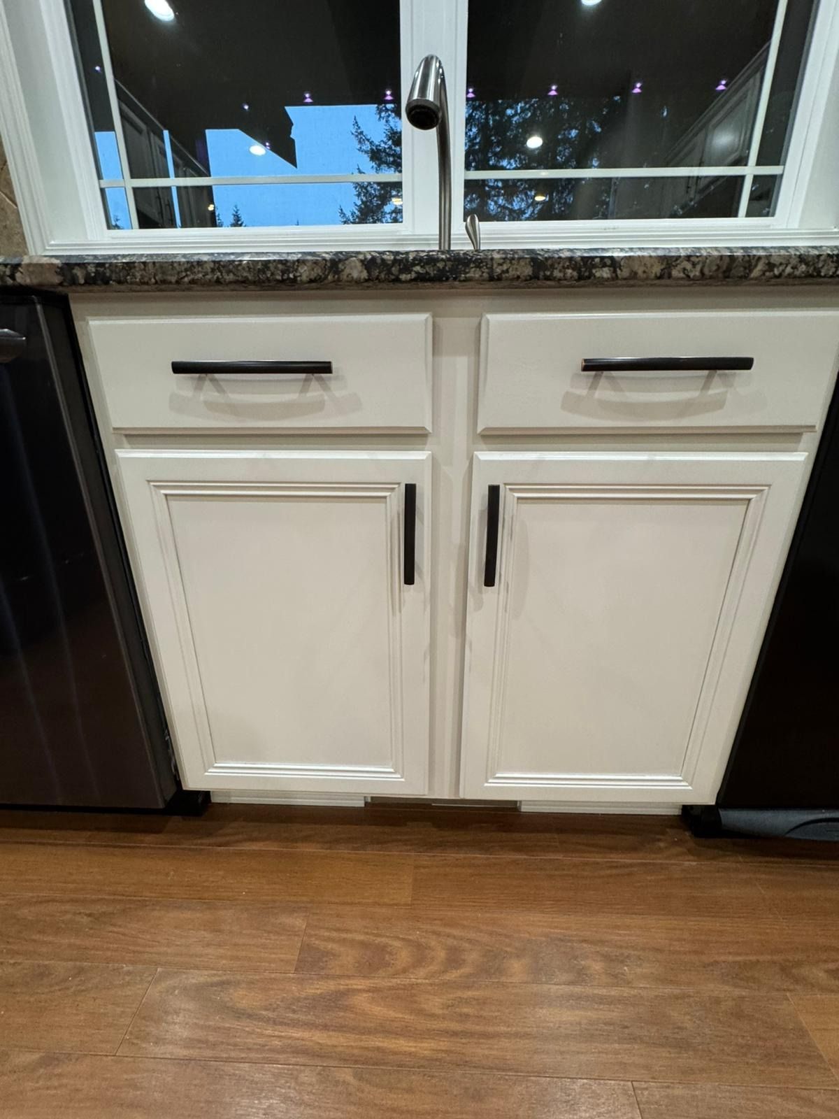 White kitchen cabinets with black handles beneath a dark granite countertop and a silver faucet.