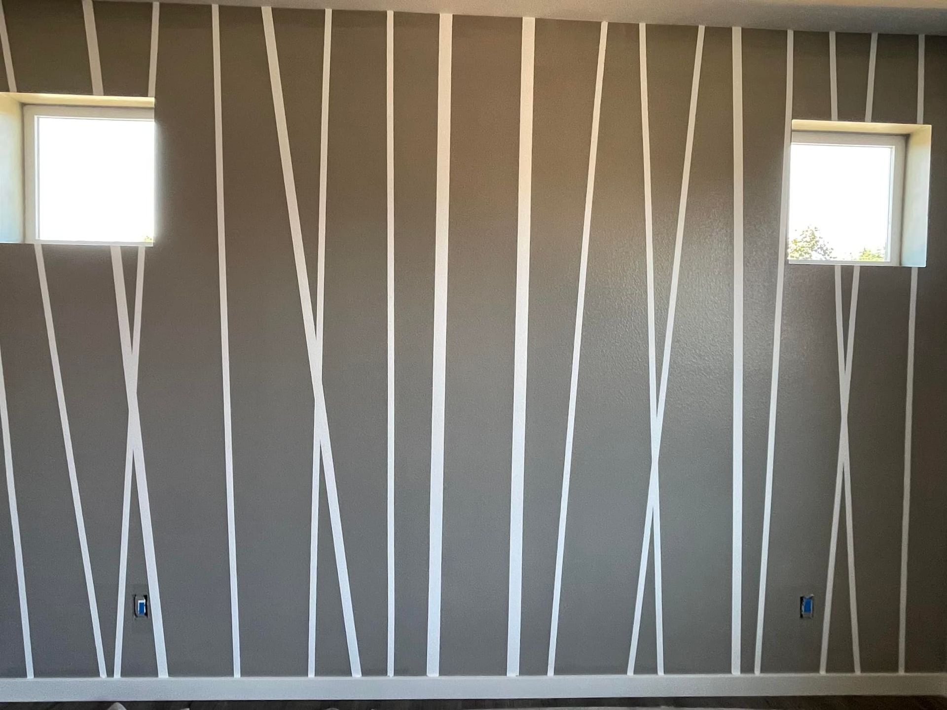 An interior wall painted brown with vertical white stripes of varying widths and angles, featuring two square windows.