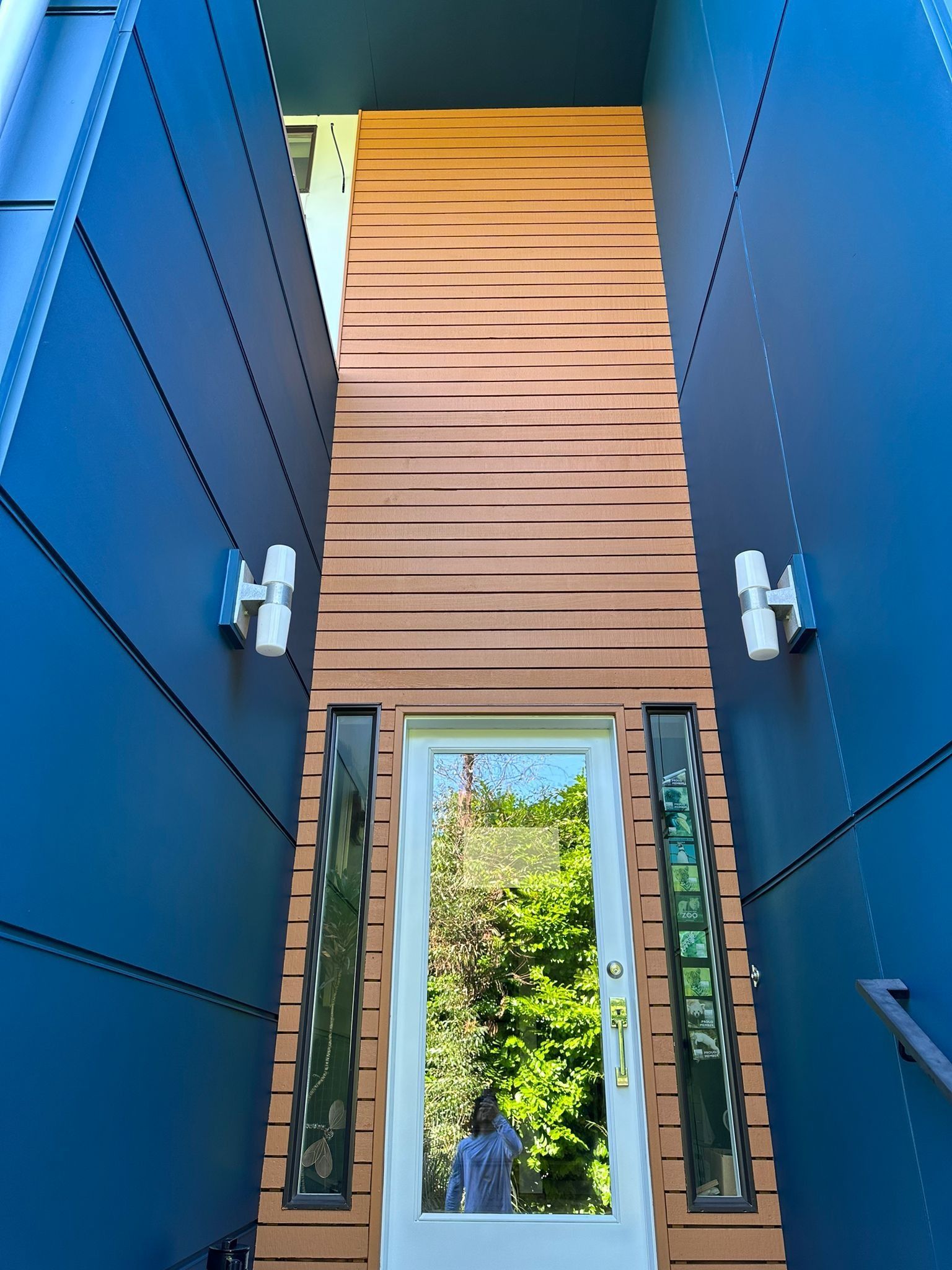 An entryway with a white door, flanked by glass sidelights, set within blue walls and a horizontal wood-slat accent wall.