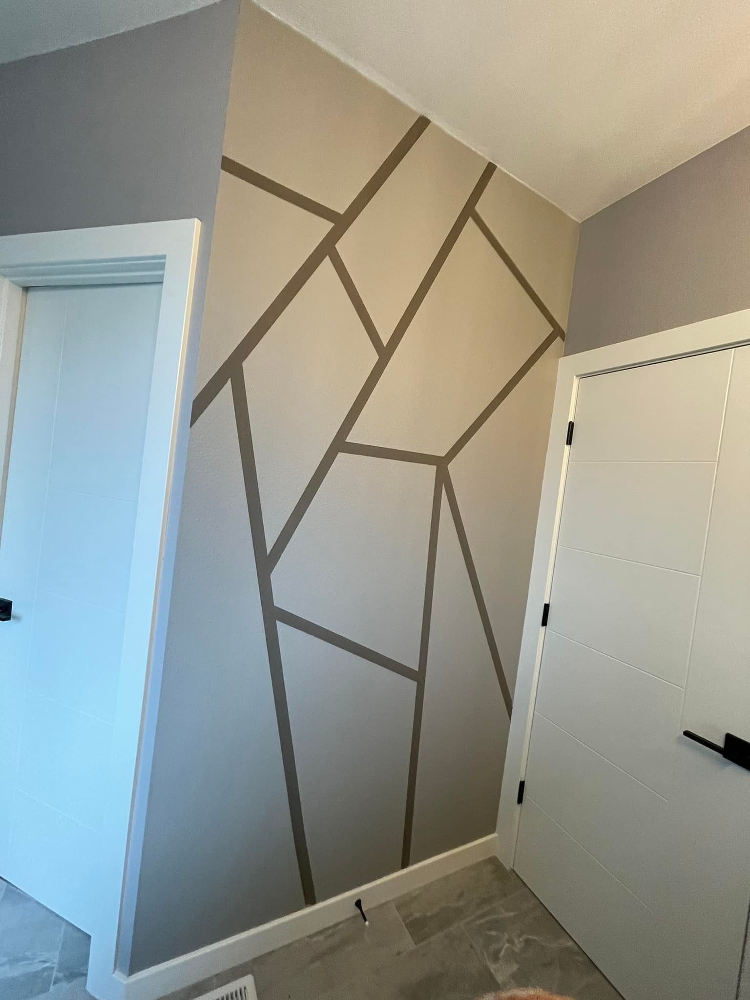 An interior wall with a tan and gray geometric design created by dark lines, positioned between two white door frames.