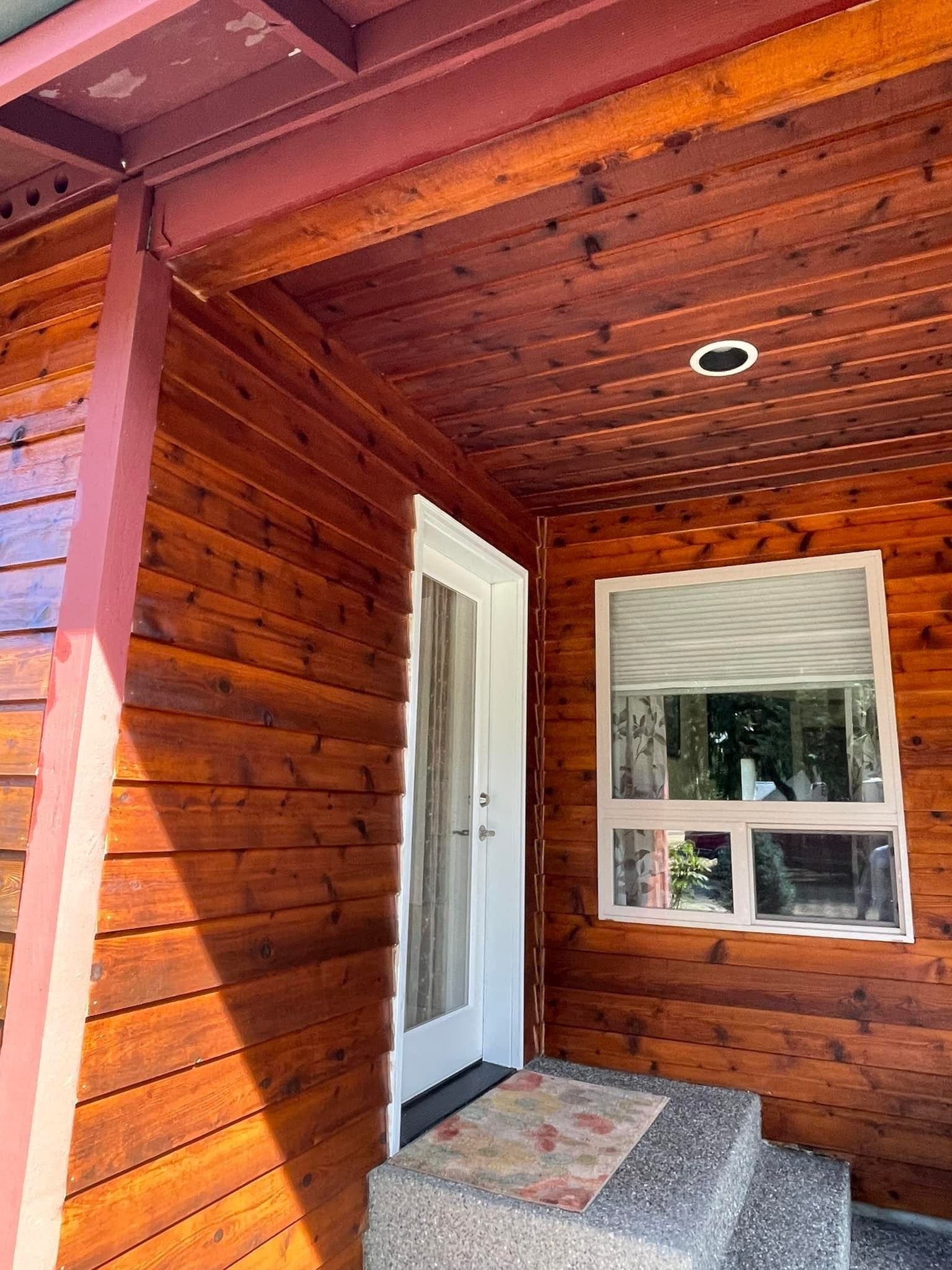 An exterior view of a house entrance featuring a white door, a single window, and steps under a wooden porch roof.
